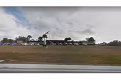 One-story nursing center building seen across a wide grassy lawn with a flagpole and cloudy sky overhead.