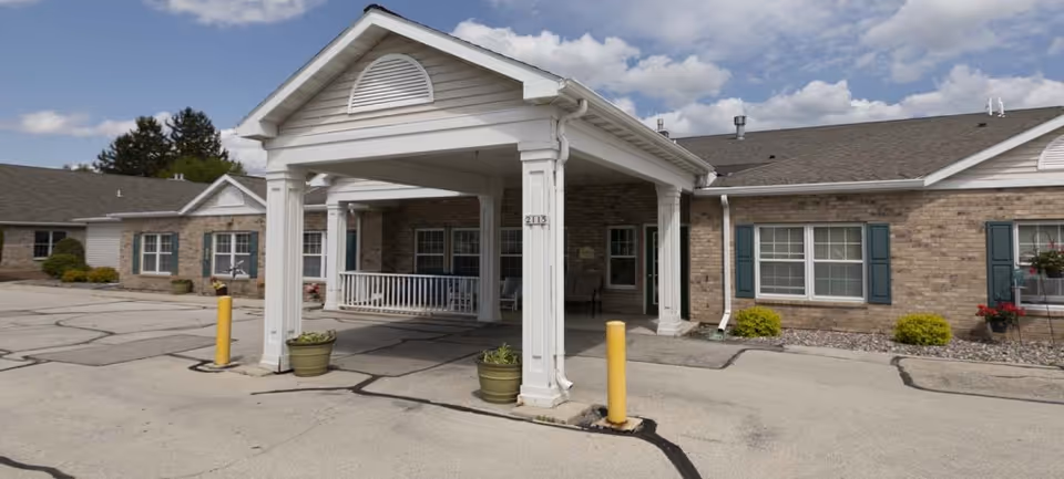 Front entrance of a single-story brick assisted living building with a covered porte-cochere and paved driveway.