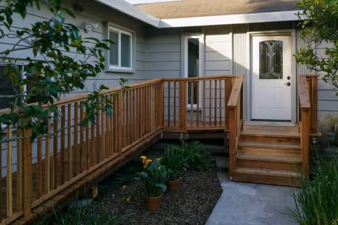 Exterior view of a gray senior living home with a wooden ramp to the front door.