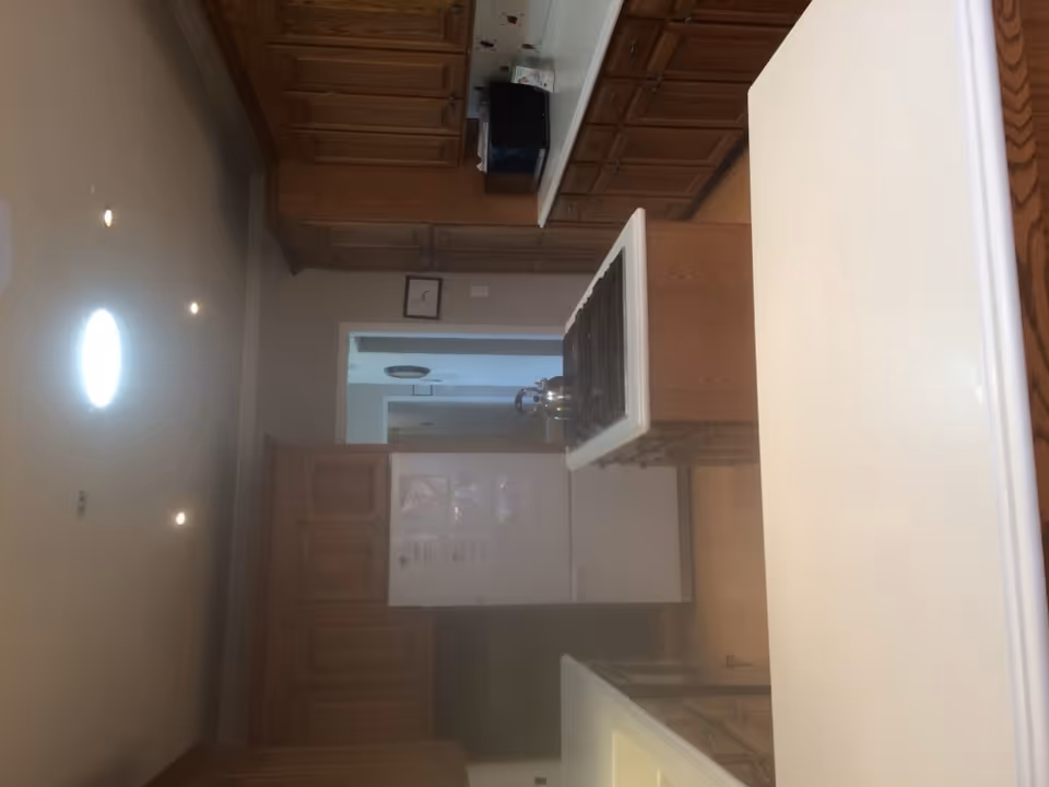 Interior view of a kitchen with wooden cabinets, white countertops, a white refrigerator, a stove with a kettle on it, and a microwave on the counter.
