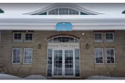 Snow-covered front entrance of a beige brick building with glass double doors and a 'Prairie View' sign above.