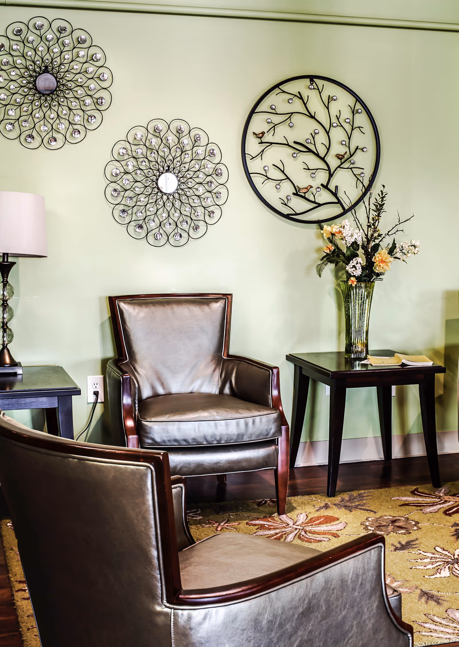 Two leather armchairs and side tables in a seating area with decorative wall art and a vase of flowers.