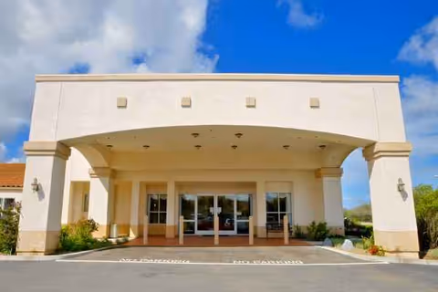 Front view of a beige senior living facility entrance under a curved porte-cochere.