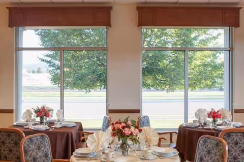 Dining room in a senior living facility with round tables and floral centerpieces.
