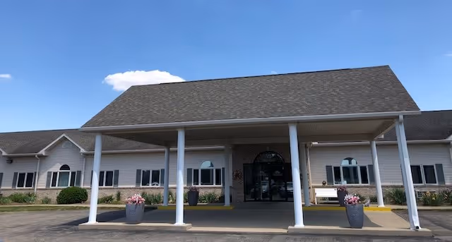 Front exterior view of Eastland Retirement Community building with a covered entrance supported by white columns, flower pots on either side, and a clear blue sky above.