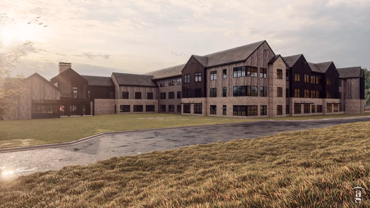 Three-story senior living building with stone and wood exterior seen from the road and front lawn at sunset.