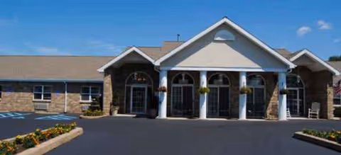 Brick and stone senior living facility entrance with arched windows and a paved driveway.