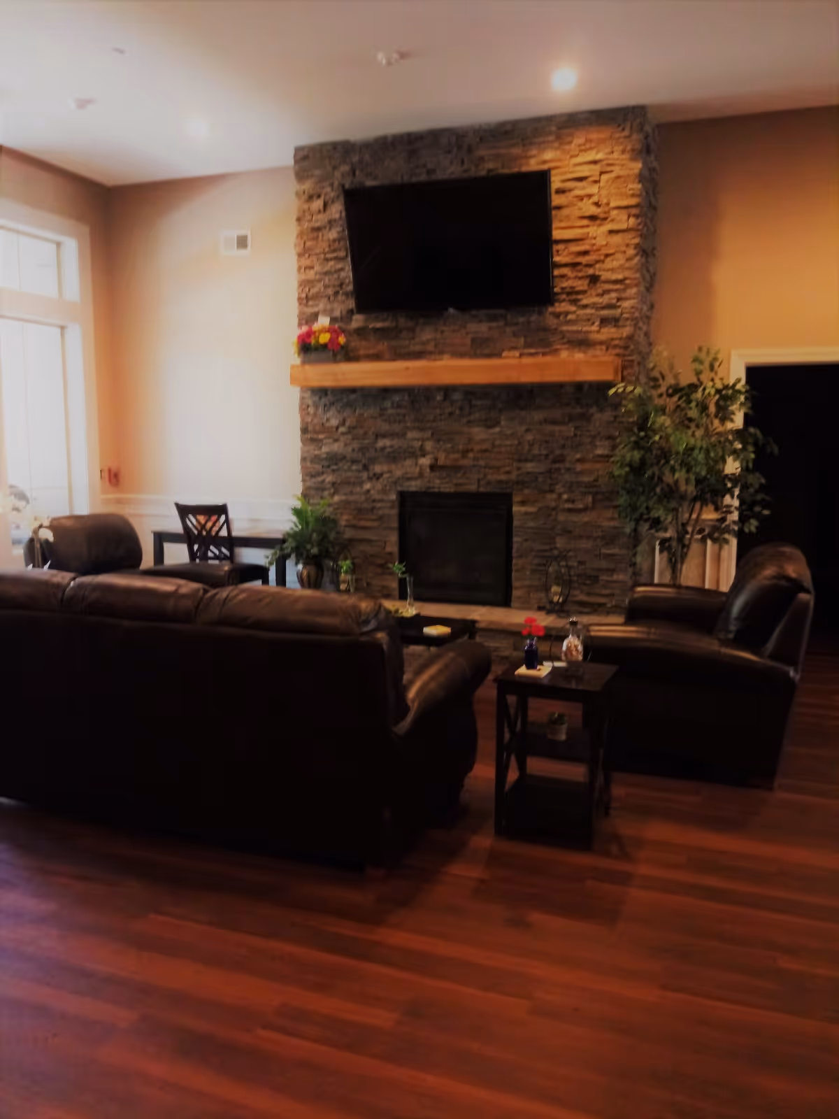 Cozy living room with leather sofas facing a stone fireplace topped by a wall-mounted TV, hardwood floors and side tables.