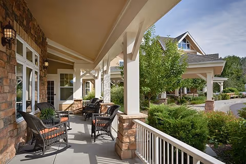 Covered front porch with wicker chairs and columns overlooking landscaped driveway and the building entrance.