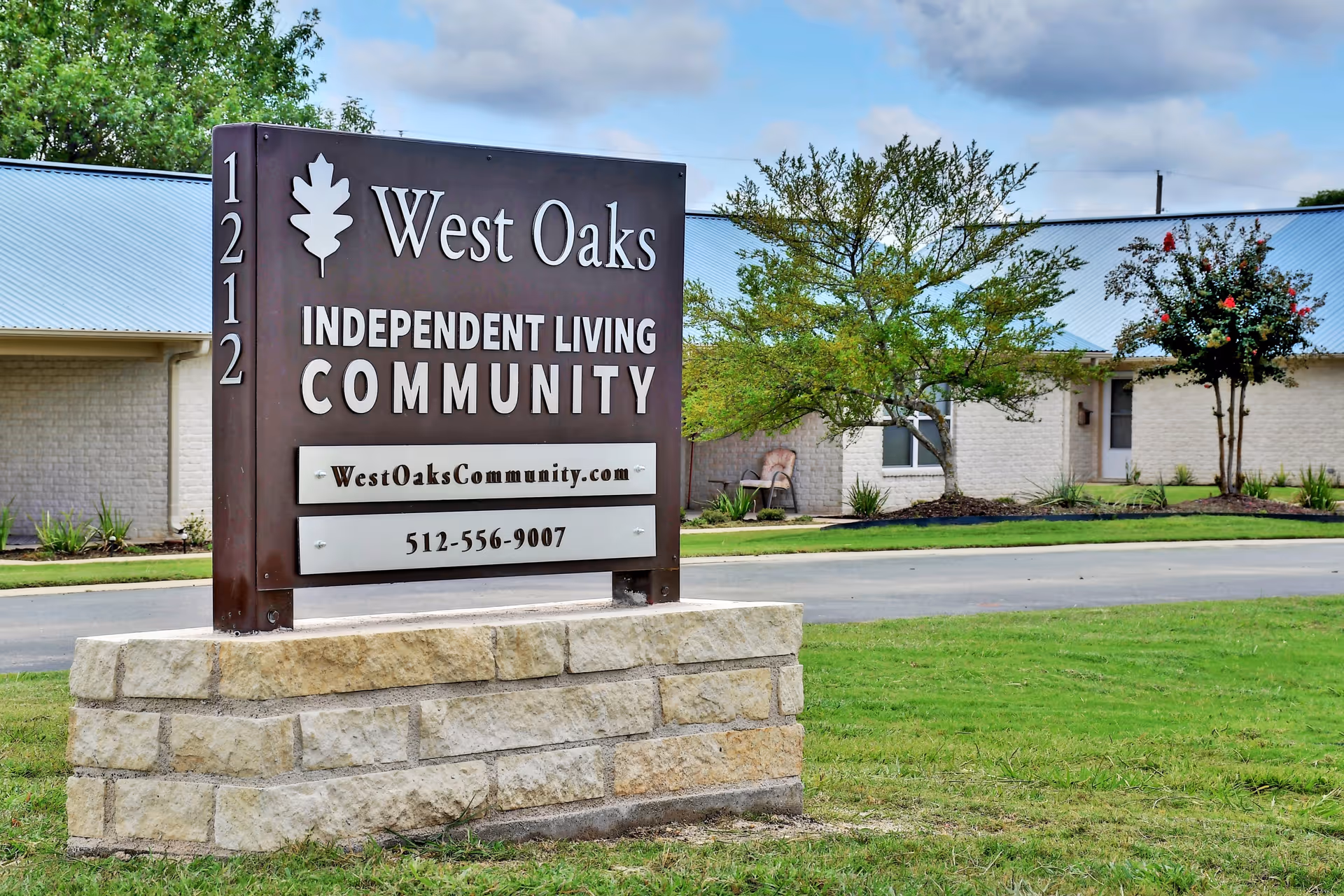 A freestanding sign reading "West Oaks Independent Living Community" stands on a stone base in front of a single-story building with trees and lawn.