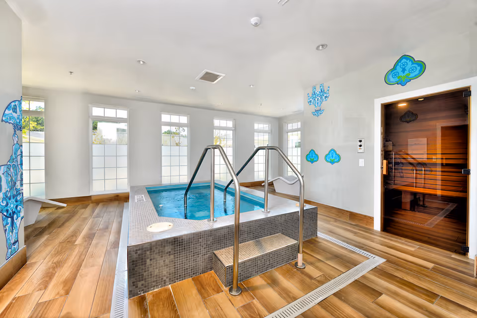 Indoor spa room with a tiled hot tub, metal handrails, wooden floors and an adjacent sauna.