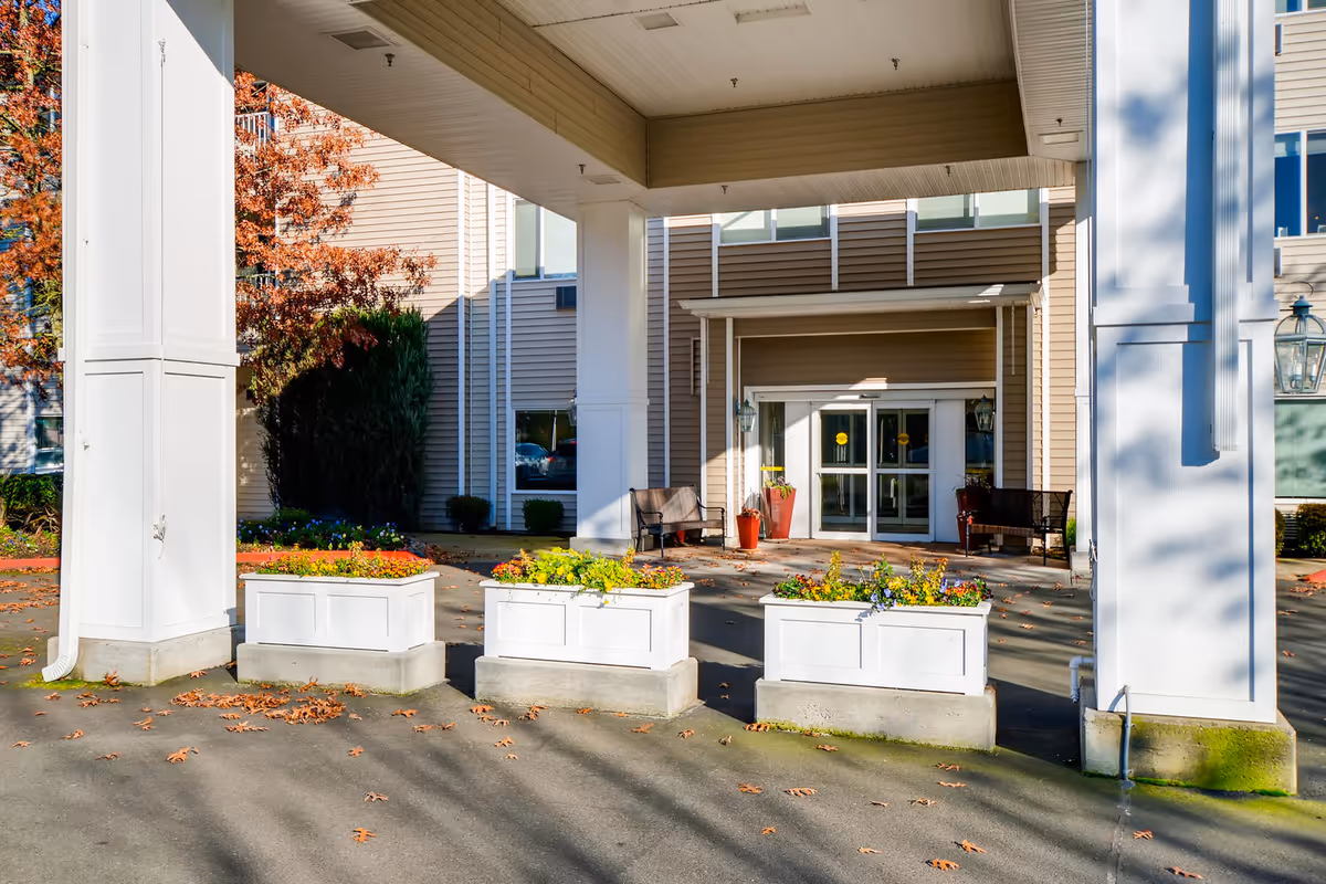 Covered entrance of Vancouver Pointe showing white columns, three planter boxes, benches and glass entry doors.