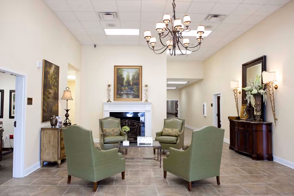 Bright seating area with four green armchairs arranged around a coffee table in front of a fireplace under a chandelier.