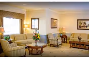 Bright communal living room with sofas, armchairs, coffee tables, lamps, and framed artwork.