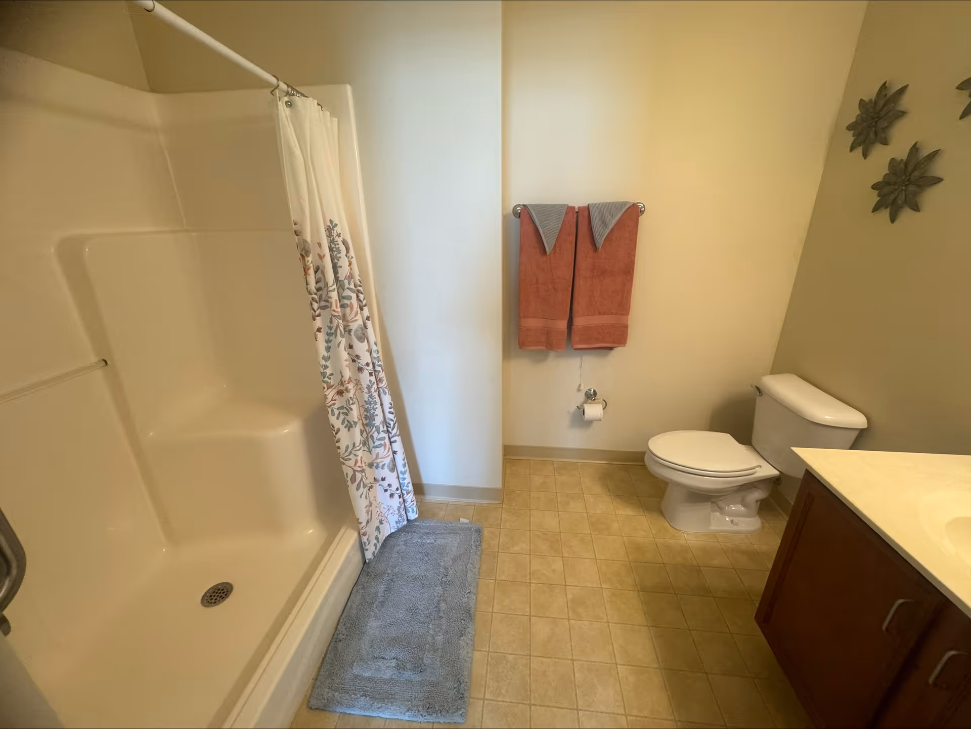 Bathroom with a shower-tub and curtain, toilet, vanity, towel rack with two towels, and a bath mat on the tiled floor.
