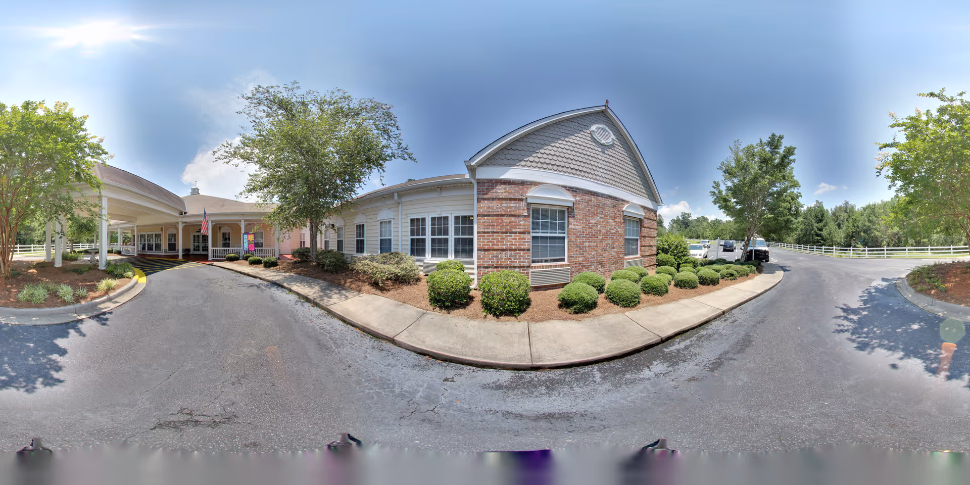 Exterior front entrance of a senior living building with a covered porte-cochere, driveway, shrubs, and an American flag.
