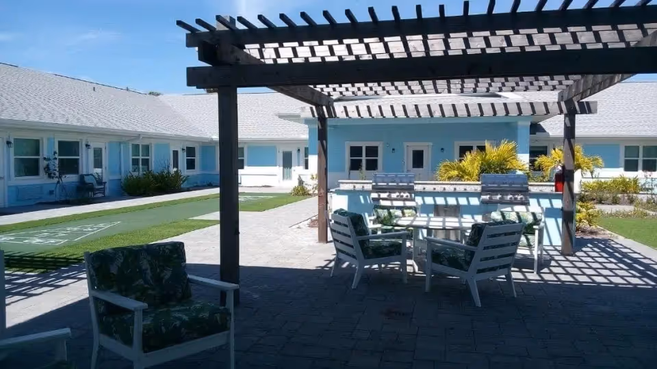 Outdoor courtyard with patio furniture under a pergola at a light blue senior living facility.
