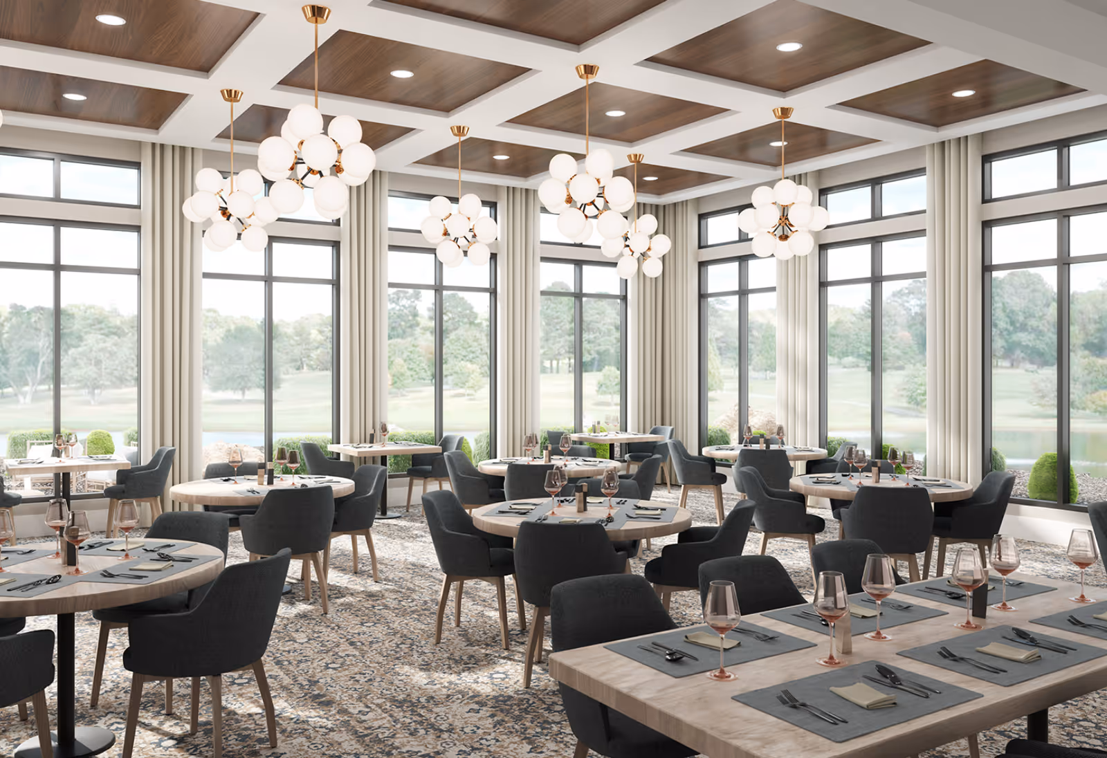 A spacious dining room with large windows offering a scenic view of greenery and trees outside. The room features multiple round and rectangular tables set with placemats, napkins, cutlery, and wine glasses. Modern chandeliers with multiple globe lights hang from a coffered ceiling with wood paneling. The floor is covered with a patterned carpet, and the chairs are upholstered in dark gray fabric.