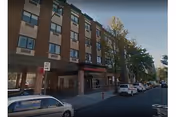 Brick five-story building on a city street with parked cars and trees.