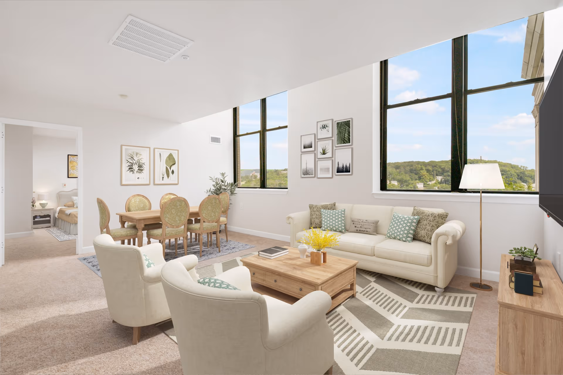 A bright and spacious living room and dining area in a senior living community. The living room features a cream-colored sofa with patterned cushions, two matching armchairs, a wooden coffee table with decorative items, and a floor lamp next to a large window with scenic views. The dining area has a wooden table with six upholstered chairs and framed botanical artwork on the wall. A bedroom is visible through an open doorway.