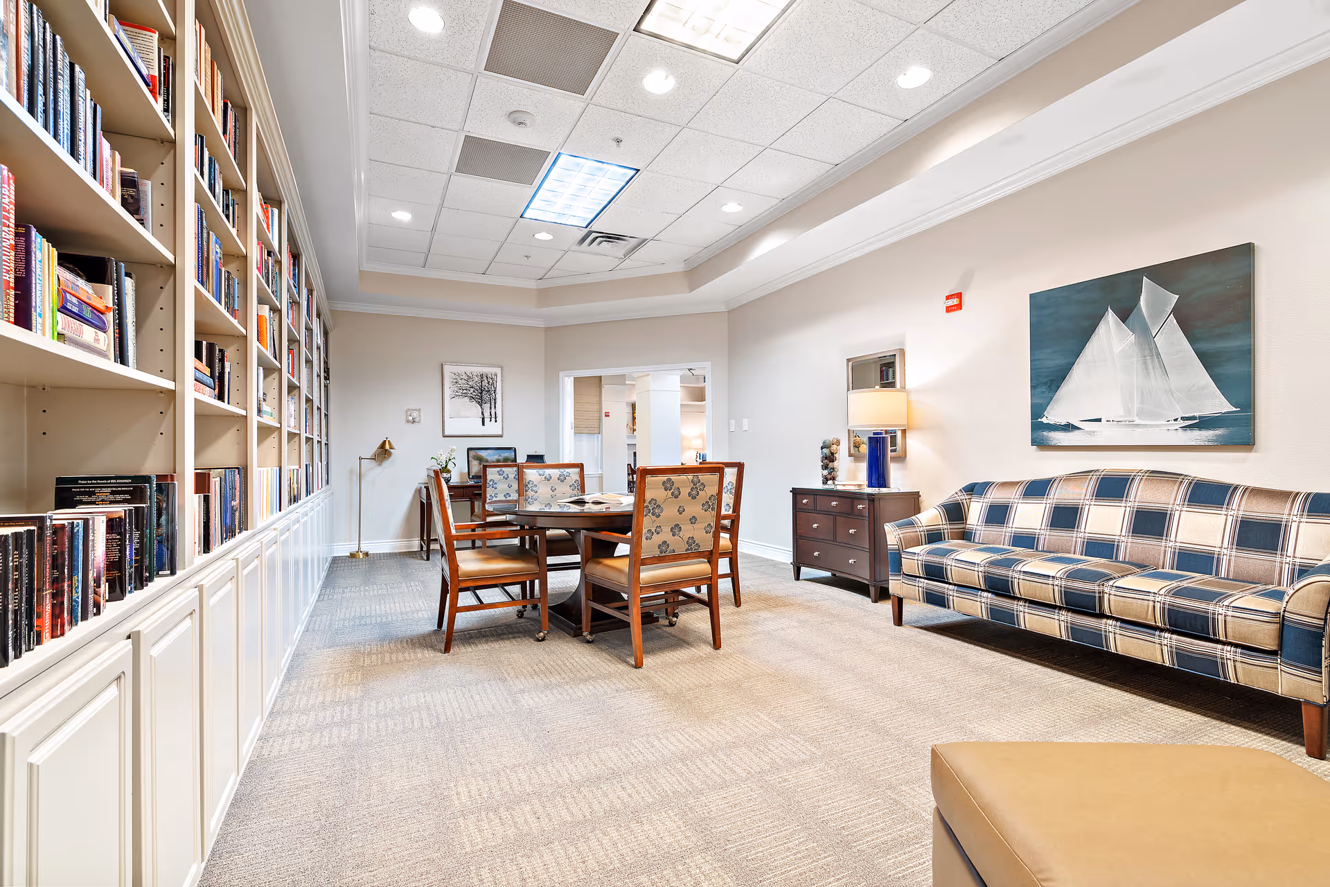 Bright common lounge with built-in bookshelves, a table and chairs, a plaid sofa, and nautical artwork on the wall.