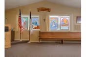 Interior room with stained-glass windows, a wooden bench/pew, two flags, and a 'Welcome' sign above.