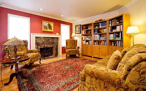 Cozy living room with fireplace, armchairs, sofa, bookshelf, and patterned rug.