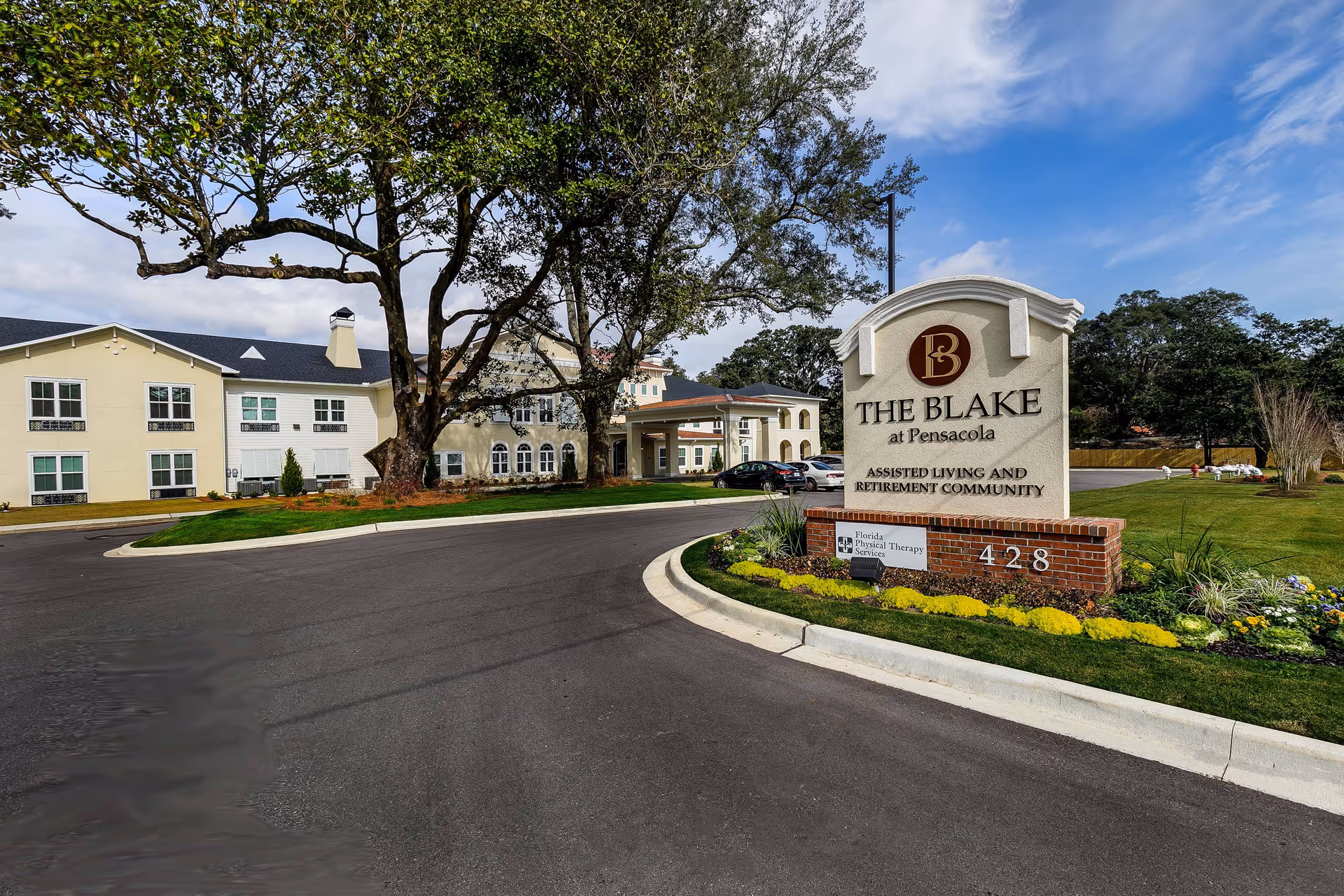 Entrance sign and driveway of The Blake at Pensacola assisted living community with the building, large oak tree, and landscaped grounds visible.