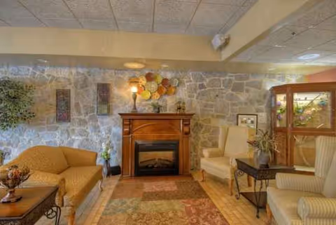 Cozy living room with stone fireplace, beige seating, plants, and wall decor.