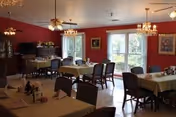 Sunlit dining room with red walls, chandeliers, and empty tables set for meals.