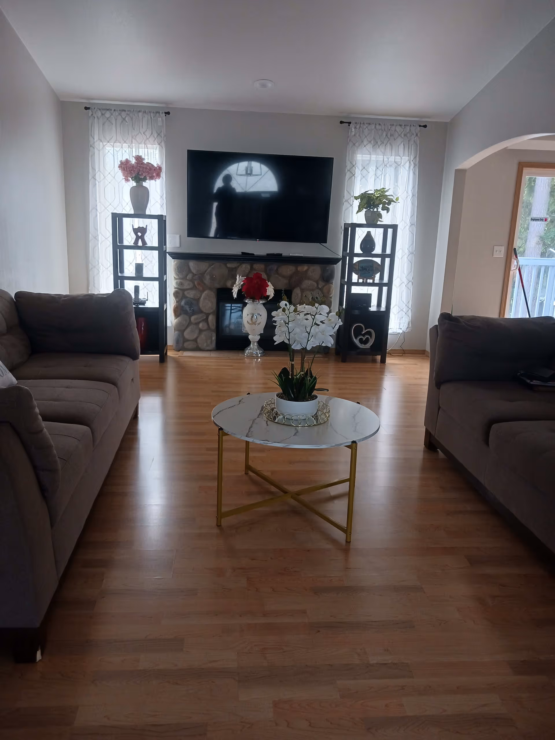 Bright living room with two sofas, a round coffee table with a potted orchid, and a TV mounted above a stone fireplace.