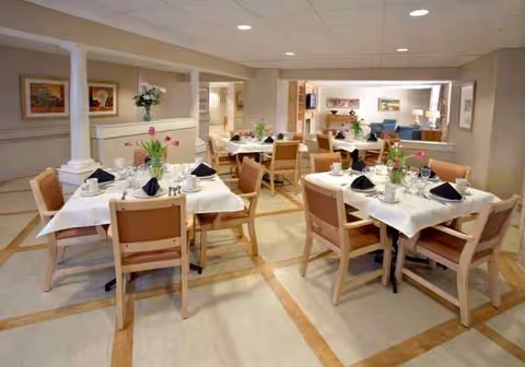 A spacious, warmly lit senior living dining room with tables set for meals.