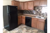 Small kitchen with a black refrigerator and dishwasher, wooden cabinets, mosaic tile backsplash, sink, and tiled floor.