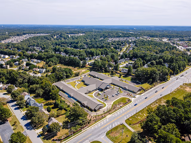 Aerial view of an assisted living facility complex surrounded by roads, parking areas, lawns, and residential neighborhoods.