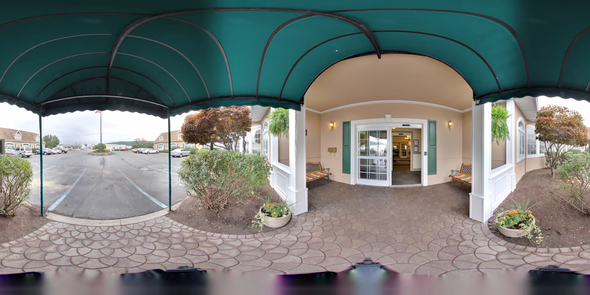 Covered entrance with a green awning, benches, and sliding glass doors opening to a parking lot.