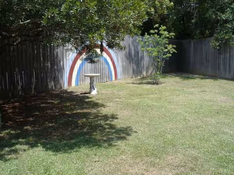 Backyard scene with a painted rainbow on a wooden fence, a birdbath, grass, and trees.