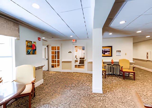 Carpeted interior common area with seating, a central column, and glass-paneled doors leading to another room.