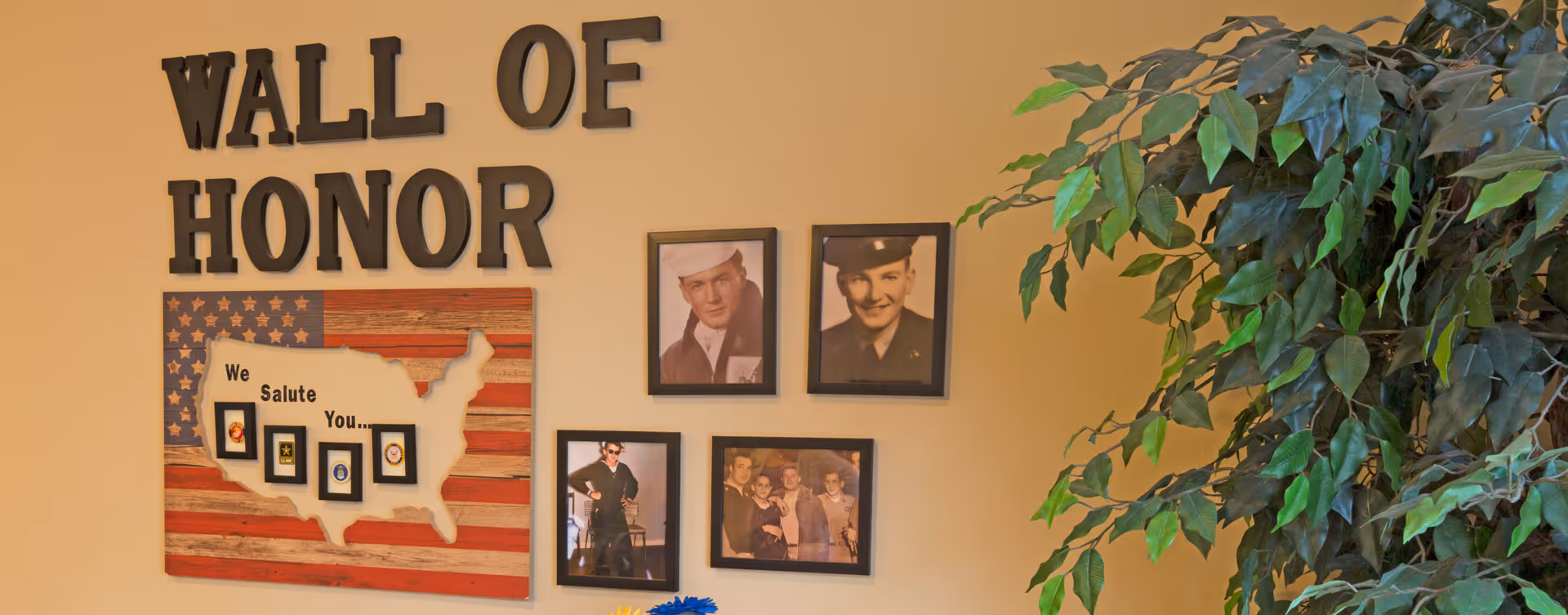 Indoor wall display titled Wall of Honor featuring photos, a U.S. map, and patriotic decor.