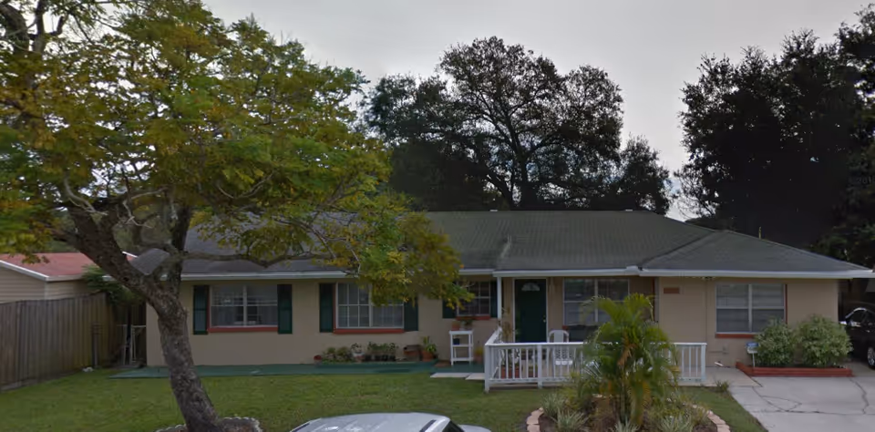 Buena Vida Residence front exterior with porch, green door, and surrounding trees.