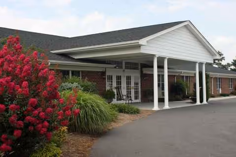 Brick assisted living facility with a white porte-cochere entrance and landscaped shrubs.