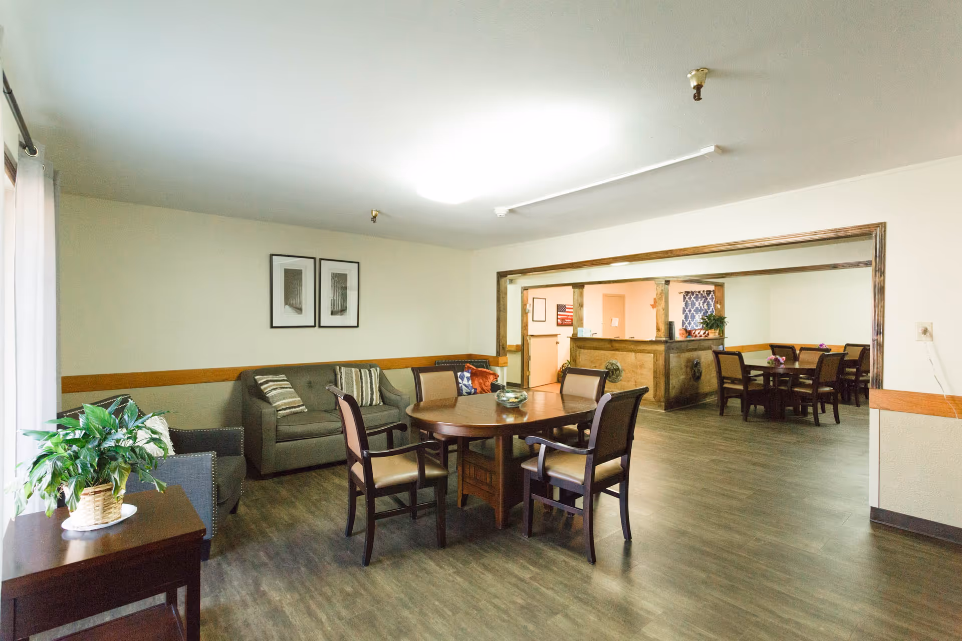 Open communal lounge and dining area with round tables and chairs, a sofa seating area, and a reception counter.