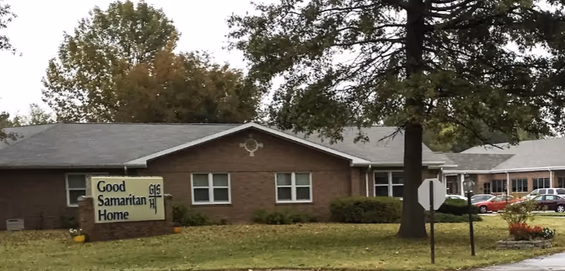 Front view of a single-story brick senior living facility with a lawn and a sign reading 'Good Samaritan Home'.