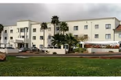 Exterior view of a three-story senior living facility named Christian Care Manor IV with palm trees and a green lawn in front under a cloudy sky.