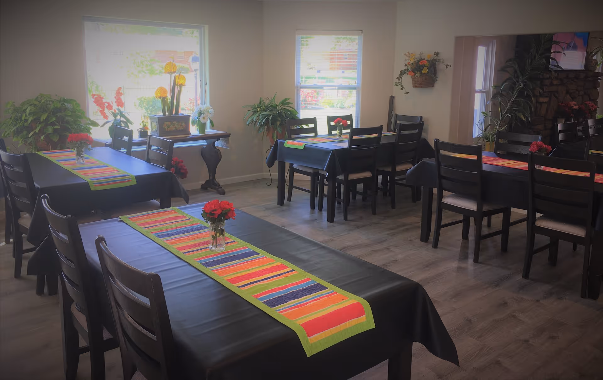 A bright dining room with multiple tables covered in black tablecloths, colorful striped runners and small floral centerpieces.
