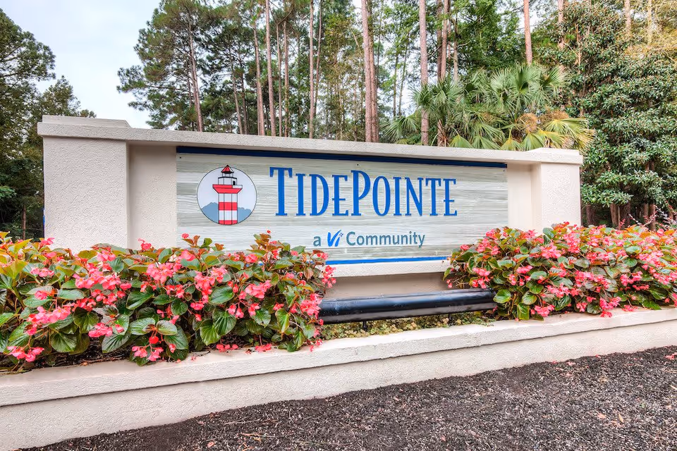 Outdoor entrance sign for TidePointe, a Vi Community, surrounded by pink flowers and greenery with tall trees in the background.