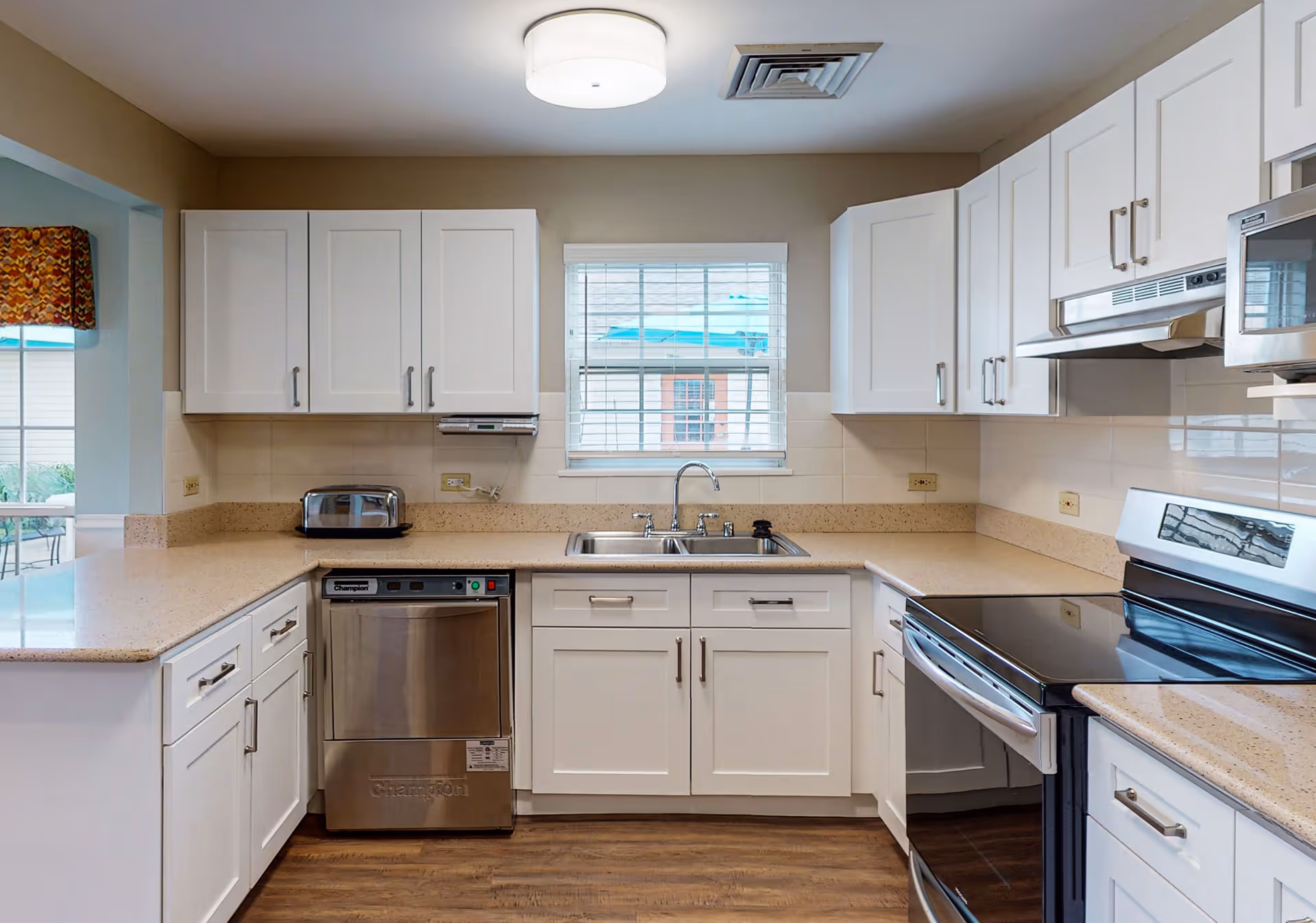 Bright modern kitchen with white cabinets, stainless appliances, a sink under a window and beige countertops.