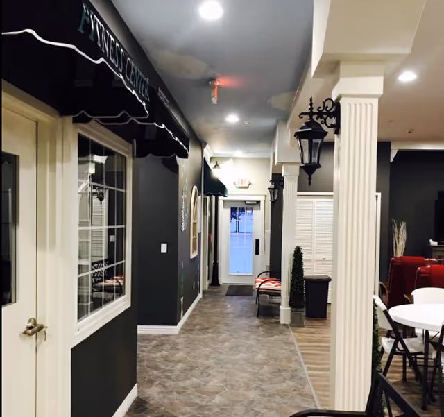 Interior hallway of a senior living facility with columns, wall lanterns, seating and a door at the far end.