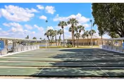 Outdoor shuffleboard courts with benches along the sides, palm trees in the background, and a partly cloudy blue sky above at Buccaneer Mobile Estates.