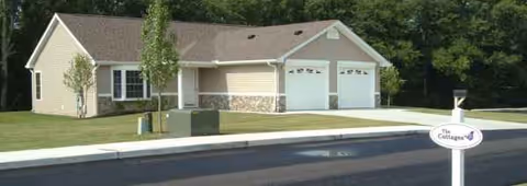 Suburban single-story beige building with two garage bays, manicured lawn, and a street sign.