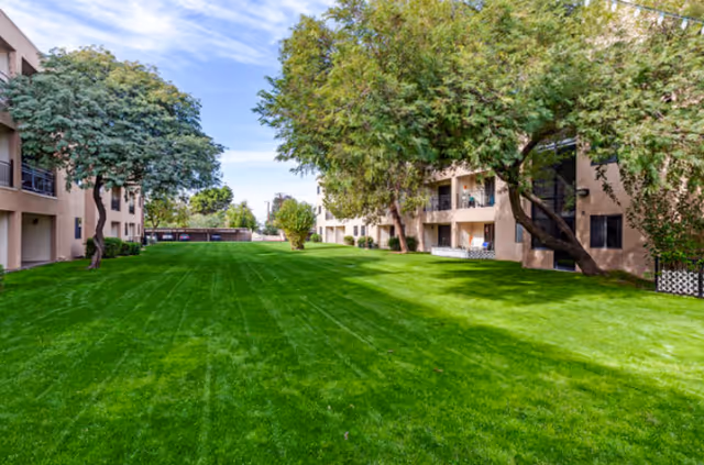 Lush green lawn between senior living buildings with shaded trees on a sunny day.